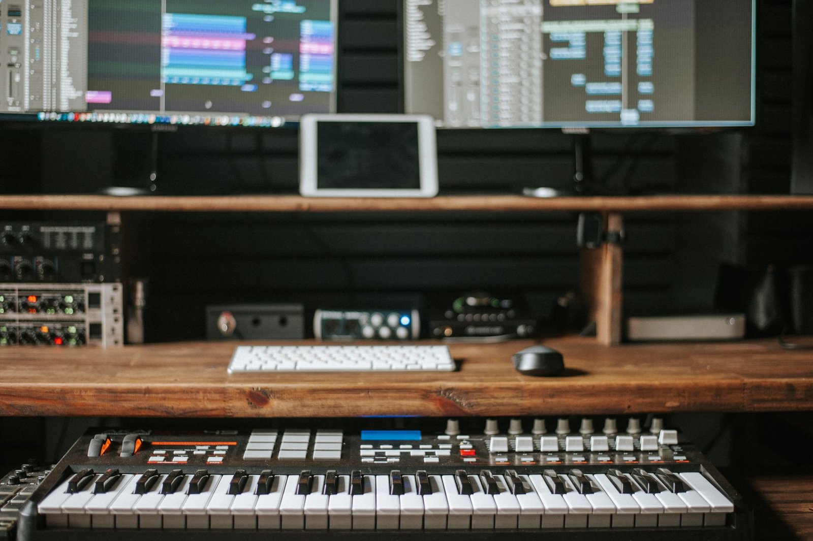 Mesa de producción musical con teclado MIDI y pantallas de un DAW