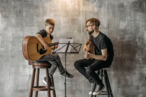 Niño aprendiendo a tocar la guitarra clásica con la ayuda de un profesor
