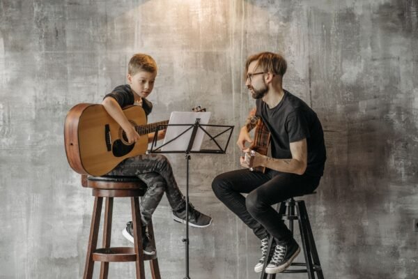 Niño aprendiendo a tocar la guitarra clásica con la ayuda de un profesor